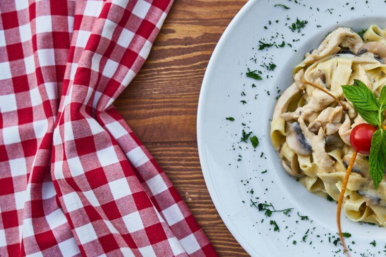 A rich and creamy fettuccine pasta with mushrooms garnished with herbs and a cherry tomato.